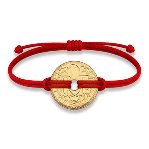 Peut inclure: Un bracelet en cordon rouge avec un pendentif en forme de pièce d'or. La pièce a un trou au centre et des motifs complexes autour des bords.