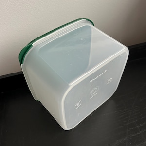May include: A clear, square food storage container with a green lid. The container has rounded corners and is made of translucent plastic. The brand name is visible on the side.