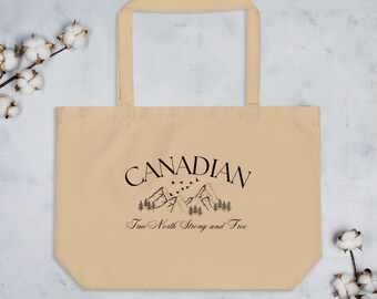 May include: Beige tote bag with black text and graphic. The word "CANADIAN" is arched above a mountain range and trees. Below the graphic is the text "True North Strong and Free". The bag has two handles.