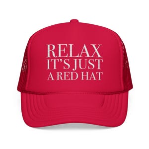 May include: A red trucker hat with white text that reads "RELAX IT'S JUST A RED HAT". The hat has a mesh back and a curved brim. The hat is a vibrant red color.