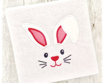 May include: A white felt bunny face with pink ears and a red nose. The bunny has black whiskers and black eyes.