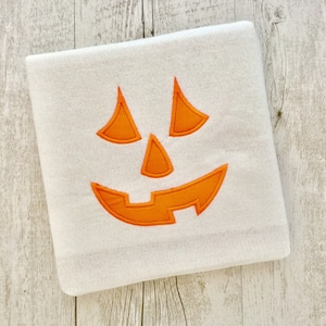 May include: White fleece blanket with an orange embroidered jack-o'-lantern face.