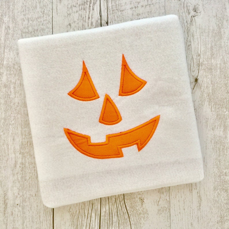 May include: White fleece blanket with an orange embroidered jack-o'-lantern face.
