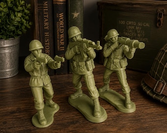 Könnte beinhalten: Drei olivgrüne Plastiksoldaten-Figuren, die auf individuellen Sockeln stehen. Der erste Soldat hält eine kleine Pistole, der zweite ein Gewehr und der dritte eine Panzerabwehrwaffe. Jede Figur trägt einen Helm und eine detaillierte Uniform.