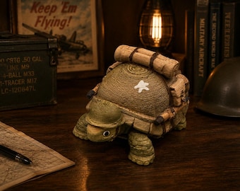 Könnte beinhalten: Eine Schildkrötenfigur mit einem grünen Helm im Militärstil, einem strukturierten Panzer mit weißem Sternemblem und einer auf dem Rücken befestigten braunen Schlafrolle. Die Schildkröte hat einen hellgrünen Kopf, dunkelgrüne Beine und ein weißes Auge.