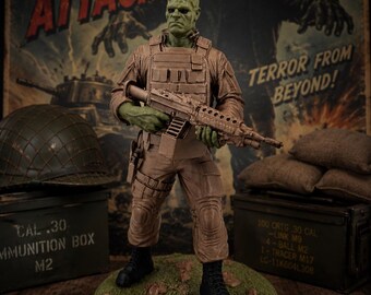 Könnte beinhalten: Eine grünhäutige Frankenstein-Monster-Figur in beigefarbener taktischer Militärausrüstung, bestehend aus Weste und Hose, die ein Gewehr hält. Die Figur steht auf einem runden grünen Sockel mit der Aufschrift FRANK vor einem alten Filmplakat.