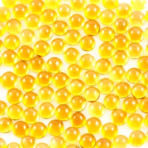 May include: A close-up image of a large quantity of small, round, translucent amber-coloured glass beads.