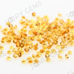 May include: A scattering of small, round, faceted, golden yellow gemstones on a white background.