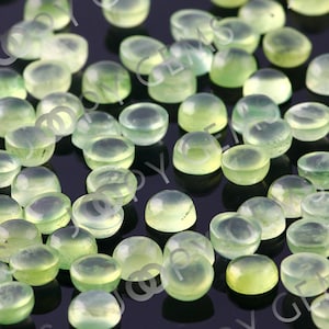 Puede incluir: Una colecci&oacute;n de piedras preciosas cabuj&oacute;n transl&uacute;cidas de color verde p&aacute;lido. Las piedras son redondas con una base plana y una parte superior abovedada, mostrando una sutil variaci&oacute;n de color. Las gemas est&aacute;n dispersas, creando un patr&oacute;n texturizado y org&aacute;nico.