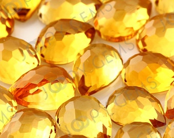 May include: A close-up of a group of faceted, pear-shaped, golden yellow gemstones. The stones are arranged in a random pattern and are all approximately the same size.
