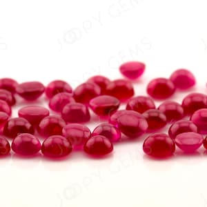 以下が含まれることがあります： 白い表面に散らばっている、丸い赤い宝石のグループ。おそらくルビーです。宝石は滑らかで磨かれており、わずかに光っています。