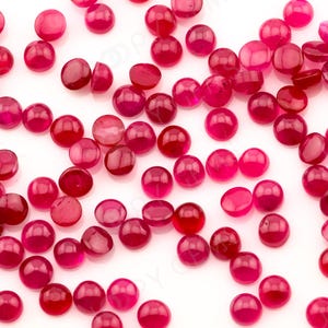 May include: A scattering of round, red cabochon gemstones on a white background. The gemstones are smooth and polished, with a deep red colour.