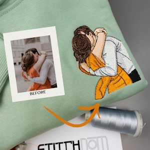 May include: A sage green sweatshirt featuring an embroidered design of two people embracing, based on a printed photograph labeled BEFORE. The embroidery depicts a person in a white shirt and a person in an orange dress. A spool of grey thread is visible.