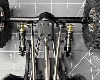 May include: Close-up of a black and silver model car chassis with suspension components and wheels. The chassis features detailed parts, including shocks, linkages, and a central drive shaft. The tires have a rugged tread pattern.