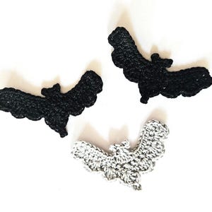 Peut inclure: Trois décorations de chauve-souris crochetées en noir et gris. Les chauves-souris sont faites à la main avec des formes d'ailes et de corps détaillées, parfaites pour Halloween ou les travaux manuels à thème. Les chauves-souris sont disposées sur un fond blanc.