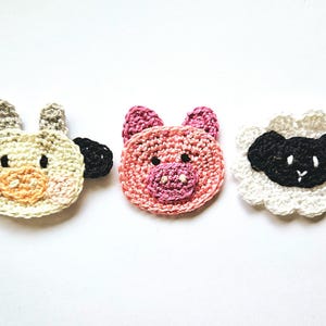 May include: Three crocheted animal appliques: a white cow, a pink pig, and a white sheep with a black face.