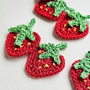 Peut inclure: Quatre appliques en crochet en forme de fraises avec des feuilles vertes et des centres jaunes. Les fraises sont rouges et les feuilles sont vertes.