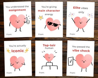May include: Six white cards with pink heart illustrations and various phrases like "You understood the assignment" and "Elite vibes only." Each card has a "From:" line. The cards are on a dark wood surface.