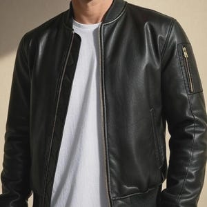 May include: Black leather bomber jacket with a ribbed collar, cuffs, and hem. The jacket features a front zipper closure and a zippered pocket on the left sleeve. A white t-shirt is visible underneath the jacket.