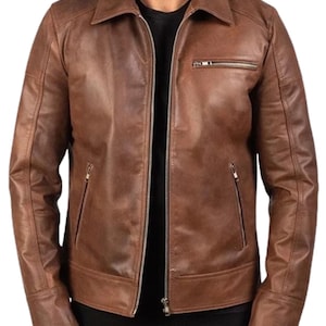 May include: A brown leather jacket with a collared neckline and a zipper closure. The jacket has two zippered pockets on the front and a small zippered pocket on the chest. The jacket is a medium brown color.