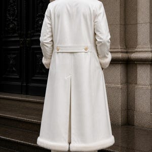 Puede incluir: Un abrigo largo blanco con cuello y pu&ntilde;os de piel. El abrigo presenta un cintur&oacute;n abotonado en la cintura y una abertura en la espalda. La persona lleva pantalones y botas blancas. Dise&ntilde;o cl&aacute;sico y elegante.