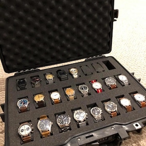 May include: A black, open watch case filled with various wristwatches. The watches have different colored faces and bands, including leather and metal. The case is lined with black foam to protect the watches.