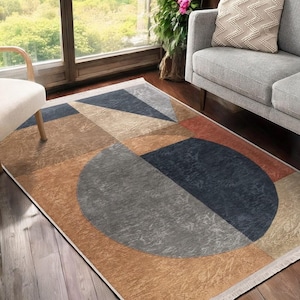 Op de afbeelding: Een geometrisch vloerkleed met een grote cirkel in het midden. Het kleed heeft een bruin, beige, grijs en blauw kleurenschema.