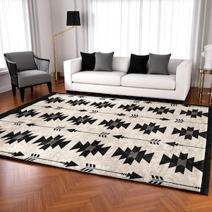 Op de afbeelding: Een geometrisch zwart-wit tapijt met een patroon van pijlen en ruiten. Het tapijt heeft een crèmekleurige achtergrond en ligt op een houten vloer.