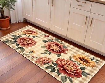 May include: A rectangular kitchen rug with a floral design. The rug features large, red and yellow flowers with green leaves set against a beige and white checkered background. The rug is placed on a wooden floor in front of white cabinets.