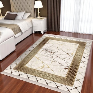 May include: A white and gold area rug with a marble pattern and a geometric border. The rug has a fringe edge.