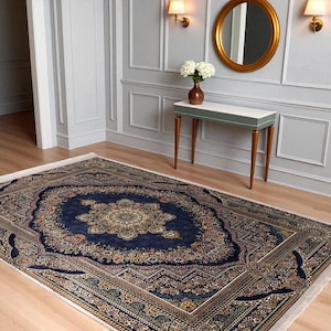 May include: A large, rectangular area rug with an intricate, ornate design. The rug features a deep blue central field with a central medallion and detailed floral patterns in shades of gold, red, and green. The border is a lighter color with similar patterns.