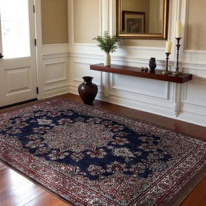 May include: A large, rectangular rug with a navy blue field and a detailed floral pattern in shades of red, cream, and beige. The rug is placed on a hardwood floor in a room with white wainscoting and a dark brown vase.