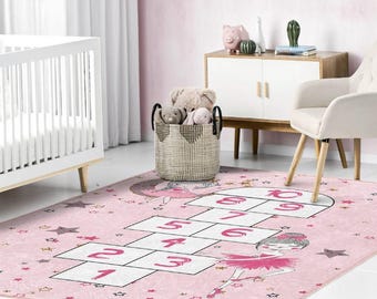 May include: Pink and white hopscotch rug with a ballerina design and gold stars. The rug features numbers 1 through 10.