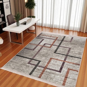 Puede incluir: Una alfombra rectangular con un diseño geométrico. La alfombra presenta un fondo gris claro con líneas que se cruzan en tonos marrón, negro y morado. Está colocada sobre un suelo de madera.