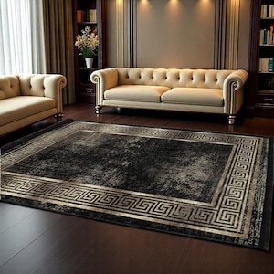 May include: A black and cream area rug with a Greek key border. The rug has a distressed, vintage look and is laid out on a hardwood floor in a living room setting.