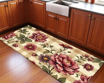 May include: A rectangular kitchen rug with a beige plaid pattern and large floral designs in shades of burgundy, purple, and cream. The rug is placed in front of a kitchen sink and cabinets.