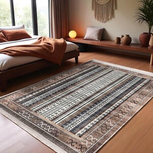 May include: Rectangular area rug with a geometric pattern in shades of brown, beige, and white. The rug features a striped design with intricate details and a border with decorative elements. The rug is placed on a wooden floor.