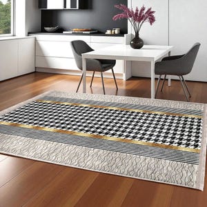 Könnte beinhalten: Rechteckiger Teppich mit schwarz-weißem Hahnentrittmuster, akzentuiert mit goldenen und schwarzen Streifen. Der Teppich hat einen cremefarbenen Rand mit einem wellenförmigen Design. Er liegt auf einem Holzboden.