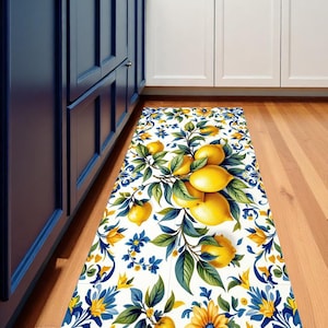 Könnte beinhalten: Ein rechteckiger Küchenteppich mit einem Zitronen- und Blumenmuster. Der Teppich hat einen weißen Hintergrund mit gelben Zitronen, grünen Blättern und blauen und gelben floralen Akzenten. Er liegt auf einem Holzboden in der Nähe von blauen und weißen Küchenschränken.