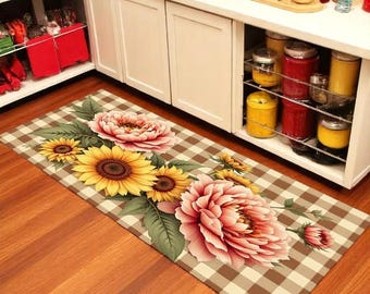 May include: A rectangular kitchen rug with a brown and white checkered pattern. The rug features a floral design with large yellow sunflowers, pink peonies, and green leaves. The rug is placed on a wooden floor.