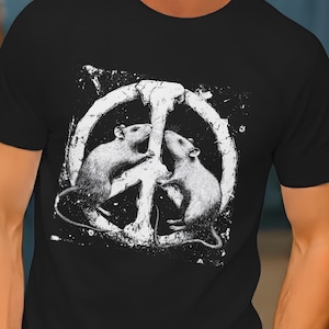 Può includere: T-shirt nero con grafica bianca raffigurante due ratti che formano il simbolo della pace. I ratti si fronteggiano all'interno del simbolo della pace. Il design ha un aspetto invecchiato e vintage. La maglietta è in materiale morbido.