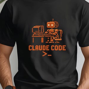 Può includere: T-shirt nero con un design arancione pixelato di un robot al computer, accompagnato dal testo "CLAUDE CODE" e un simbolo del prompt dei comandi. La maglietta è realizzata in materiale morbido, adatta per l'abbigliamento casual.