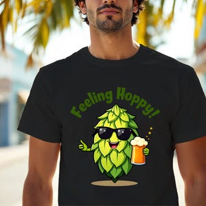 Può includere: T-shirt nera con un cartone animato di un luppolo con occhiali da sole e un boccale di birra. Il testo "Feeling Hoppy!" è stampato in verde. Il luppolo è verde e giallo.