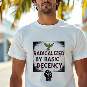 Op de afbeelding: Wit t-shirt met een grafisch ontwerp. Het ontwerp toont de tekst "RADICALIZED BY BASIC DECENCY" in een verweerde letter, een duif en een vuist. Het shirt is gemaakt van een zacht materiaal.