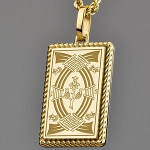 Könnte beinhalten: Goldfarbene Halskette mit rechteckigem Anhänger. Der Anhänger hat ein eingraviertes Design mit einer ovalen Form in der Mitte und dekorativen Elementen an den Rändern. Die Kette ist im Stil eines gedrehten Seils gehalten.