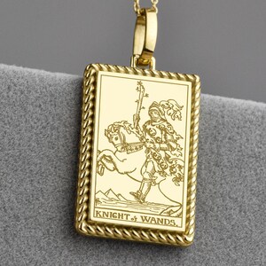 Könnte beinhalten: Goldfarbene Halskette mit einem rechteckigen Anhänger, der eine detaillierte Gravur des Tarot-Kartenmotivs Ritter der Stäbe zeigt. Der Anhänger ist von einem seilartigen Rand umgeben und hängt an einer zarten Kette mit kleinen Kugelakzenten.