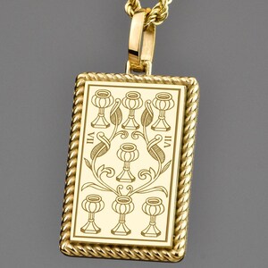 Könnte beinhalten: Eine goldfarbene Halskette mit einem rechteckigen Anhänger. Der Anhänger hat ein detailliertes Design mit einem seilartigen Rand und einem zentralen Design aus Kelchen und floralen Elementen. Die Kette ist ebenfalls goldfarben und hat ein gedrehtes Seildesign.