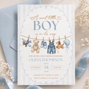 Könnte beinhalten: Eine Babyparty-Einladungskarte mit hellblau gestreiftem Hintergrund. Sie zeigt eine Wäscheleine mit einem Spielzeugflugzeug, Teddybären, blauen Babyschuhen, Jeanslatzhose, einem Holzhund und einer Haube. Der Text lautet: A sweet little BOY is on his way.