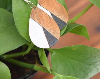 May include: A pair of teardrop-shaped wooden earrings with a geometric design. The earrings are painted in black, white, and brown.