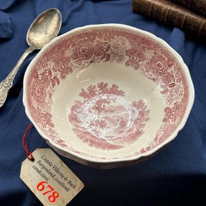 Può includere: Una ciotola in ceramica vintage con un dettagliato design floreale e paesaggistico in rosso e bianco. La ciotola ha un bordo smerlato e un'etichetta attaccata con testo. Un cucchiaio d'argento è appoggiato accanto alla ciotola.